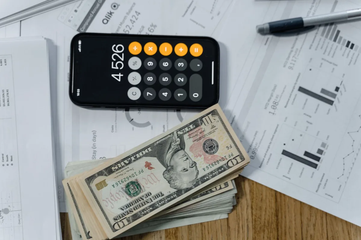 Cash, a calculator and a printed cost sheet laid out on a desk