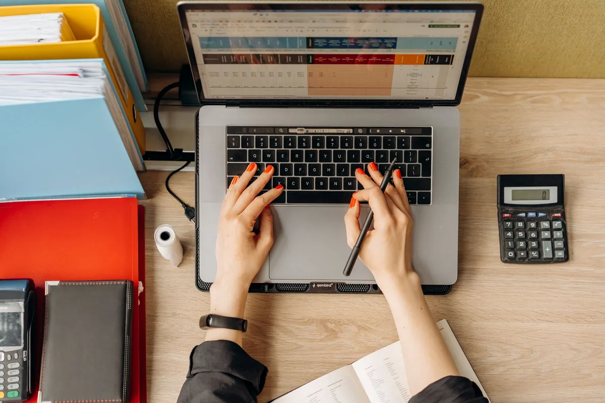 Digital Marketing Agency | ZenWeb Malaysia Hands typing on a laptop beside folders and a calculator while costing a launch