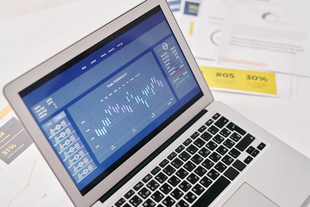 A laptop beside printed cost documents on a desk