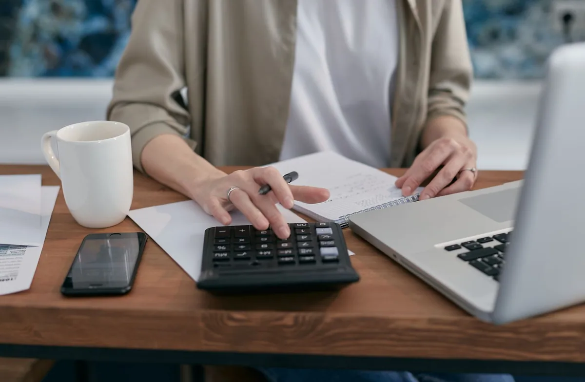 Digital Marketing Agency | ZenWeb Malaysia A person working out budget figures on a calculator beside a laptop and notebook